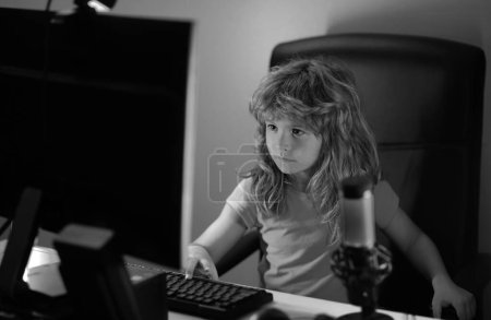 Téléchargez les photos : Enfant apprenant en ligne la nuit, en utilisant un ordinateur de bureau dans le salon à la maison. Petit hacker, jeune programmeur - en image libre de droit