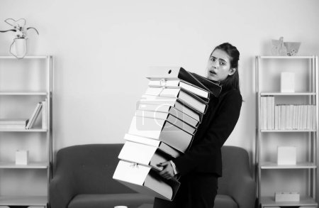 Busy young businesswoman, frustration secretary girl working overtime. Secretary accountant woman working alone late in office, holding many folders with the documents