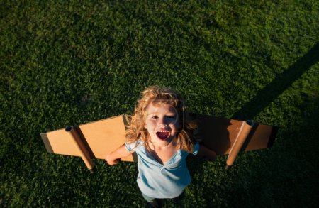 Foto de Niño risueño viajero con alas de mochila. Niño jugando piloto aviador y sueños al aire libre en el parque - Imagen libre de derechos