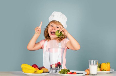 Téléchargez les photos : Portrait de chef enfant dans un chapeau de cuisinier tenir les épinards. Cuisson à la maison, gamin préparant des aliments à partir de légumes et de fruits. Une alimentation saine - en image libre de droit