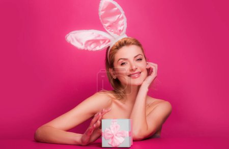 Téléchargez les photos : Femme heureuse avec boîte cadeau et oreilles de lapin à la célébration de Pâques, isolé sur rose - en image libre de droit