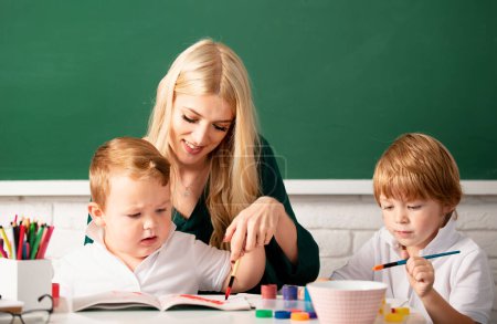 Photo for Portrait of schoolkids and teacher talking at school lesson. Happy family. Mother and two son together draw, paint. Mom helps the children boys - Royalty Free Image