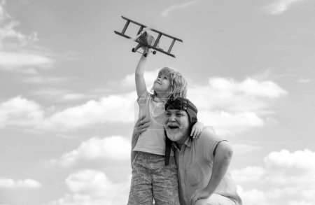Téléchargez les photos : Enfant garçon et grand-père jouant avec l'avion ensemble sur le ciel bleu. Enfant mignon avec grand-père jouant en plein air. Générations âges - en image libre de droit