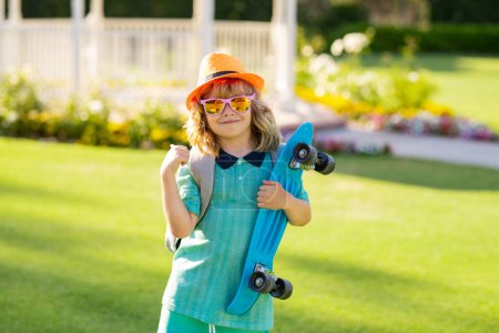 Téléchargez les photos : Enfant skateboarder dans le skate park. Petit garçon avec skateboard. Enfance, loisirs, concept de style de vie. Portrait élégant enfant avec planche à roulettes en plein air - en image libre de droit