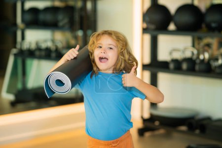 Photo for Excited kid with thumbs up holding yoga mat in gym. Yoga child concept. Young strong sporty kid. Workout sport concept - Royalty Free Image