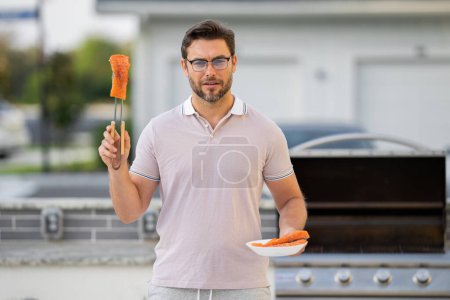 Photo for Handsome man preparing barbecue. Male cook cooking salmon fish on barbecue grill. Guy cooking meat on barbecue for summer family dinner at the backyard of the house - Royalty Free Image