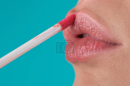 La aplicación de lápiz labial om rellenar los labios sexy. Pintura de labios con lápiz labial brillante, de cerca. Mimos, concepto de corrección de labios. Lápiz labial brillante en el labio sensual lleno regordete. Mano de mujer aplicando lápiz labial