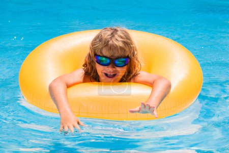 Foto de Niño en gafas de sol flotando en la piscina. Niño flotando en una piscina en vacaciones de verano. Niño feliz jugando con el anillo de natación en la piscina - Imagen libre de derechos