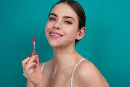 Gorgeous young woman in stylish makeup. Girl posing with new lipstick in studio. Sexy girl rouging her lips. Sexy model holding red lipstick. Applying lipstick cream balm to mouth. Red is trending