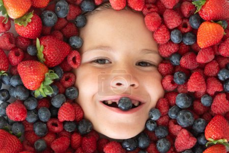 Téléchargez les photos : Alimentation saine pour les enfants. Les baies mélangent myrtille, framboise, fraise, mûre. Mélange assorti de fraise, myrtille, framboise, mûre avec fond près du visage de l'enfant - en image libre de droit