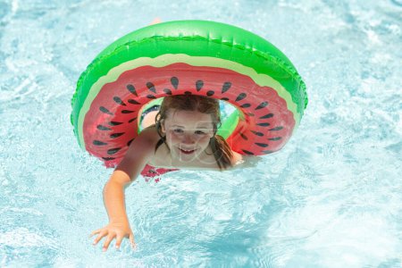 Téléchargez les photos : Enfant relaxant dans la piscine. Enfant nageant avec anneau flottant dans la piscine d'eau. Enfants drôles visage d'été - en image libre de droit