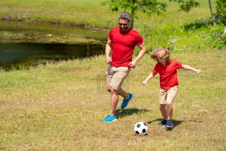 Father and son playing football in park. Dad and little boy play soccer. Sporty family enjoy summer day. Sport for kids. Football soccer game. Fathers day. Father and son kick ball on the green grass