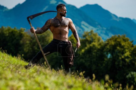 Photo for Strong muscular power sexy Man using scythe. Farmer with a scythe on green grass field. Guy cut grass. Rural farmer on summer meadow mowing grass with classic traditional scythe - Royalty Free Image