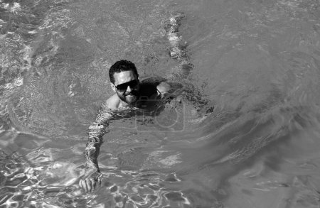 Téléchargez les photos : Homme en vacances d'été. Un type aux lunettes de soleil qui nage dans la piscine. Station balnéaire estivale - en image libre de droit