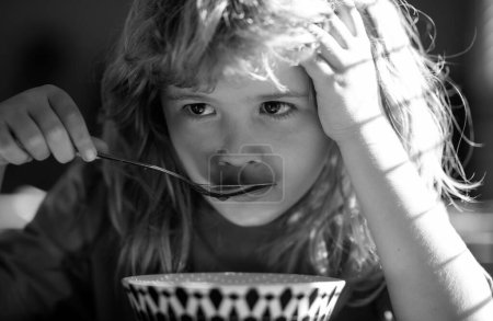 Téléchargez les photos : Unhappy sad child boy with spoon eats itself. Kid eating food on kitchen - en image libre de droit
