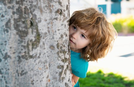 Photo for Kids games. Playing hide and seek. Peekaboo. Little boy hiding by tree - Royalty Free Image