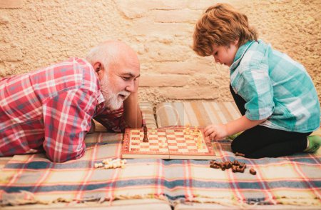 Foto de Un niño jugando al ajedrez con su abuelo. Pasatiempos de ajedrez - abuelo con nieto en un ajedrez de juego - Imagen libre de derechos