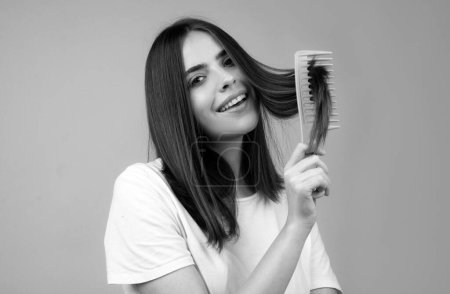 Téléchargez les photos : Femme souriante brossant les cheveux avec un peigne. Belle fille peigner les cheveux longs avec une brosse à cheveux - en image libre de droit