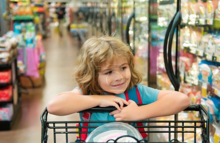 Téléchargez les photos : Enfant à l'épicerie ou au supermarché avec des marchandises dans le chariot - en image libre de droit