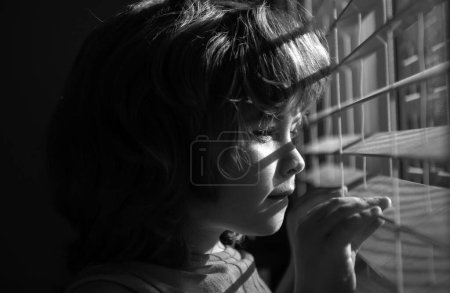 Téléchargez les photos : Enfant regardant par la fenêtre. Concept Qarantine. Protégez-vous. Restez à la maison dans l'isolement. COVID-19 Verrouillage. Pandémie de coronavirus - en image libre de droit