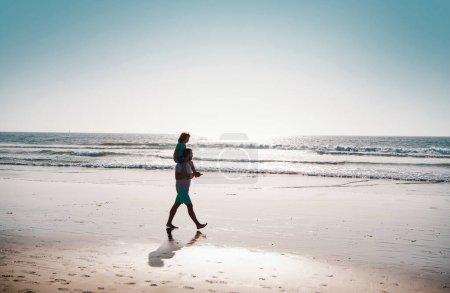 Foto de Hombre guapo padre llevando un hijo joven. Feliz padre sosteniendo al niño. Padre e hijo caminando en la playa de verano. Concepto de infancia y crianza - Imagen libre de derechos