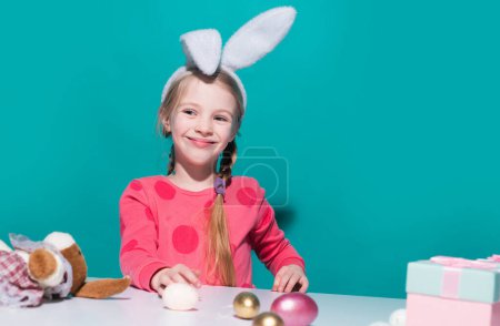 Foto de Lindo niño pequeño con orejas de conejo en el día de Pascua. Chica sonriente sosteniendo cesta con huevos pintados - Imagen libre de derechos