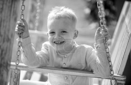 Téléchargez les photos : Enfant garçon s'amuser sur une balançoire. Adorable petit enfant qui s'amuse sur une balançoire extérieure. Enfant blond, visage émotionnel souriant - en image libre de droit
