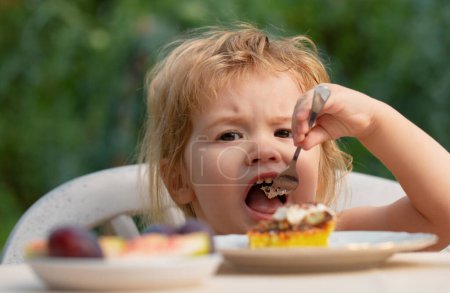 Téléchargez les photos : Un bébé qui mange du gâteau. Enfant manger cupcake à l'extérieur - en image libre de droit