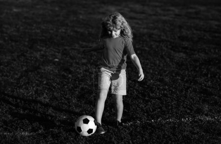 Téléchargez les photos : Soccer enfant jouer au football. Un gamin qui frappe un ballon de foot sur une pelouse. Enfant sportif pendant l'entraînement de football - en image libre de droit