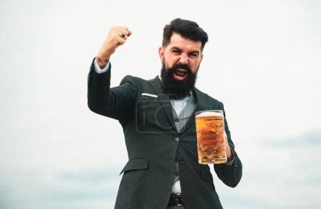 Téléchargez les photos : Homme drôle en costume classique tenant le verre avec de la bière à la main. Homme excité avec de la bière. Brasseur barman avec des émotions d'expression - en image libre de droit