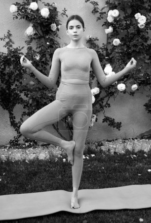 Foto de Deporte fitness mujer estirándose antes del entrenamiento. Modelo de ajuste femenino. Mujer yogui practicando yoga, ejercicio vrksasana. Estiramiento y motivación. Entrenamiento al aire libre - Imagen libre de derechos