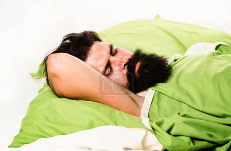 Téléchargez les photos : Violations du sommeil et de l'éveil. Jeune homme dormant sur des oreillers souples dans son lit à la maison. Homme hipster barbu ayant des problèmes de sommeil - en image libre de droit