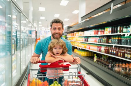 Foto de Feliz padre e hijo sonriente con carrito de compras comprando comida en la tienda de comestibles o supermercado - Imagen libre de derechos