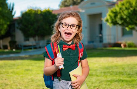 Aufgeregter Schüler mit Rucksack und Buch. Porträt eines Schülers vor der Grundschule. Nahaufnahme gesicht von glücklich schoolboy outdoor