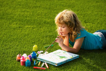 Téléchargez les photos : Des enfants artistes. Des écoliers dessinent dans un parc d'été, peignent de l'art. Petit peintre dessiner des images en plein air - en image libre de droit