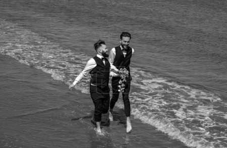 Foto de Boda de pareja gay. Lgbt matrimonio gay pareja tener romántico momento juntos. Dos hombres gay después de la boda en una playa de mar. Concepto de LGBTQ. Hombres gay caminando en una playa, tomados de la mano - Imagen libre de derechos