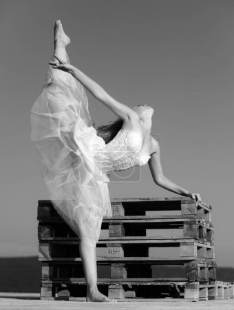 Téléchargez les photos : Ballet d'art. Une fille souple qui se sépare les jambes. Jeune belle femme en tenue de sport faisant des étirements avant l'entraînement en plein air. Adapter le corps et la vie mentale saine - en image libre de droit