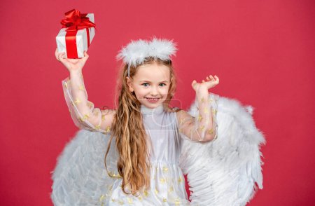 Téléchargez les photos : Joyeux ange souriant, isolé sur rouge. Petit enfant angélique ludique. Enfants de Noël - en image libre de droit