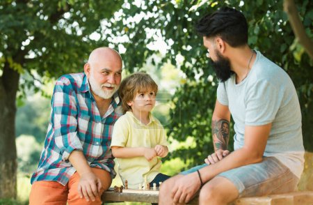 Feliz tres generaciones de hombres se divierten y juegan al Ajedrez en el parque verde. Guapo abuelo y nieto están jugando ajedrez mientras pasan tiempo juntos al aire libre
