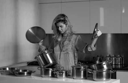 Téléchargez les photos : Femme au foyer cuisinant à la cuisine. Femme a préparé la nourriture le matin avec la casserole de cuisson. Femme de maison surmenée - en image libre de droit