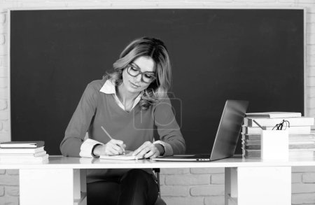Photo for Female teacher. Portrait of teacher or female tutor working at table in college or high school. Young women student studying in class - Royalty Free Image