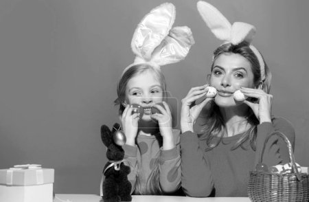 Mother and daughter in bunny ears on Easter Holding eggs, isolated on blue