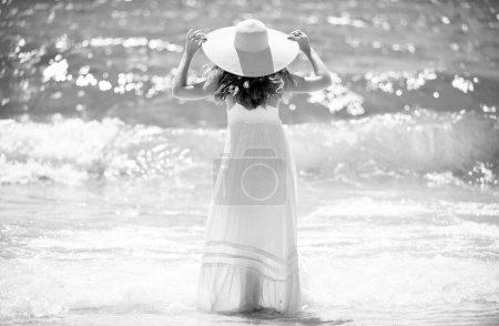 Téléchargez les photos : Vue arrière de la jeune fille attrayante avec un corps parfait sur la plage tropicale d'été. Femme sexy sur la mer, modèle féminin sensuel posant près de fond de l'océan avec espace de copie - en image libre de droit
