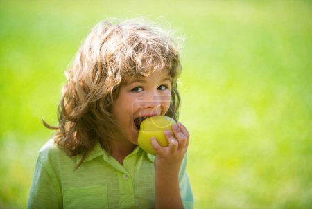 Téléchargez les photos : Petit enfant mignon mangeant de la pomme verte. Portrait d'un enfant mangeant et mordant une pomme. Bon appétit. Alimentation saine et concept enfant - en image libre de droit