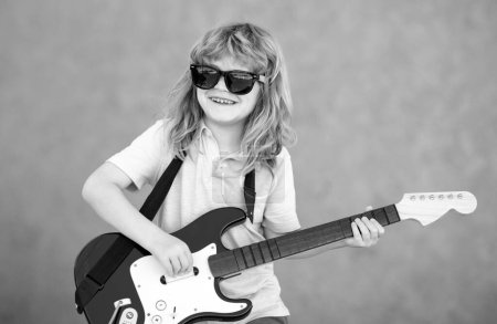 Téléchargez les photos : Garçon guitariste. Enfant rock drôle avec guitare. Petit garçon en lunettes de soleil. Concept musical pour enfants - en image libre de droit