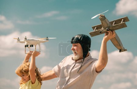 Photo for Old grandfather and young child grandson with plane and quadcopter drone over blue sky and clouds background. Men generation granddad and grandchild - Royalty Free Image