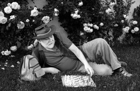 Téléchargez les photos : Vieil homme dans le jardin de printemps avec des échecs. Concept de passe-temps. Bonne vieillesse - en image libre de droit
