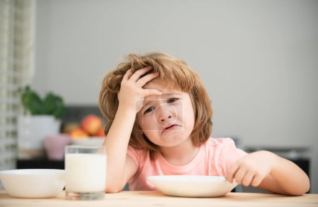 Téléchargez les photos : Malheureux enfant assis à la table à la maison cuisine n'ont pas d'appétit. Blanc tout-petit enfant garçon manger soupe saine dans la cuisine - en image libre de droit
