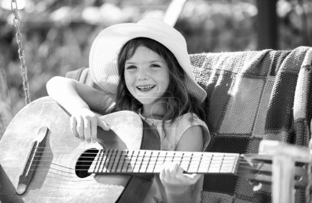 Téléchargez les photos : Joyeux sourire enfant fille jouer de la guitare. Musique et chansons pour enfants. Enfant souriant jouant à l'extérieur en été - en image libre de droit