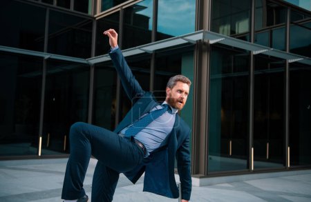 Photo for Excited businessman keeping arms raised and expressing positivity while standing outdoors with office building. Dancing businessman. To stay on top - Royalty Free Image